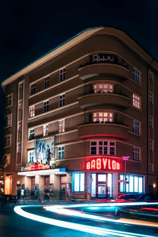 Kino Babylon bei Nacht mit roter Leuchtschrift und Lichtspuren vorbeifahrender Autos