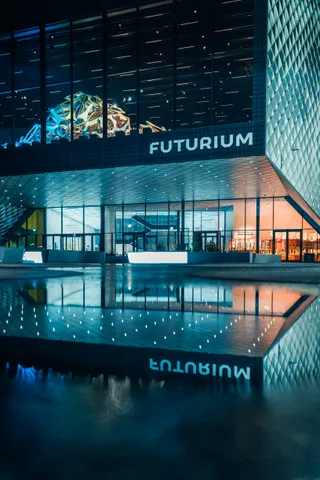 Futurium in Berlin bei Nacht, die Glasfassade spiegelt sich in einer Pfütze
