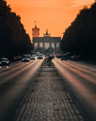 Brandenburger Tor bei Sonnenaufgang am Ende einer langen Allee, mit Radfahrer und Autos