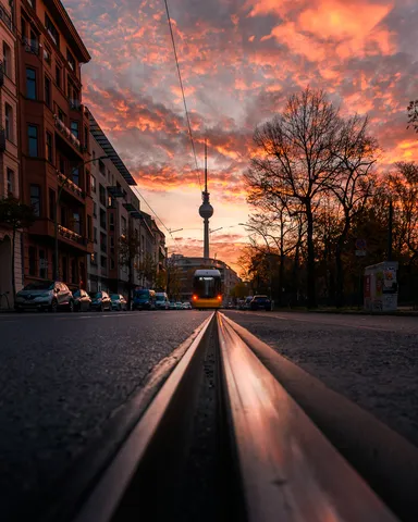 Berliner Fernsehturm bei Sonnenaufgang unter rotem Himmel, gesehen über eine Straße mit Straßenbahnschienen