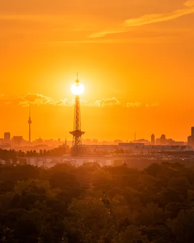 Berliner Funkturm vor der aufgehenden Sonne, dahinter Skyline und Fernsehturm