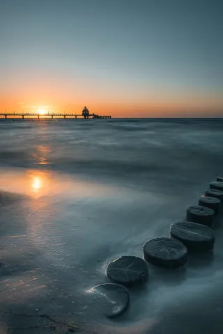 Sonnenuntergang über der Ostsee bei Zingst mit Seebrücke und Holzpfählen im Wasser